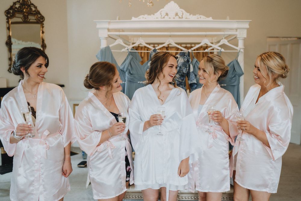 Group wearing matching white robes gather for a celebratory moment during wedding preparation.