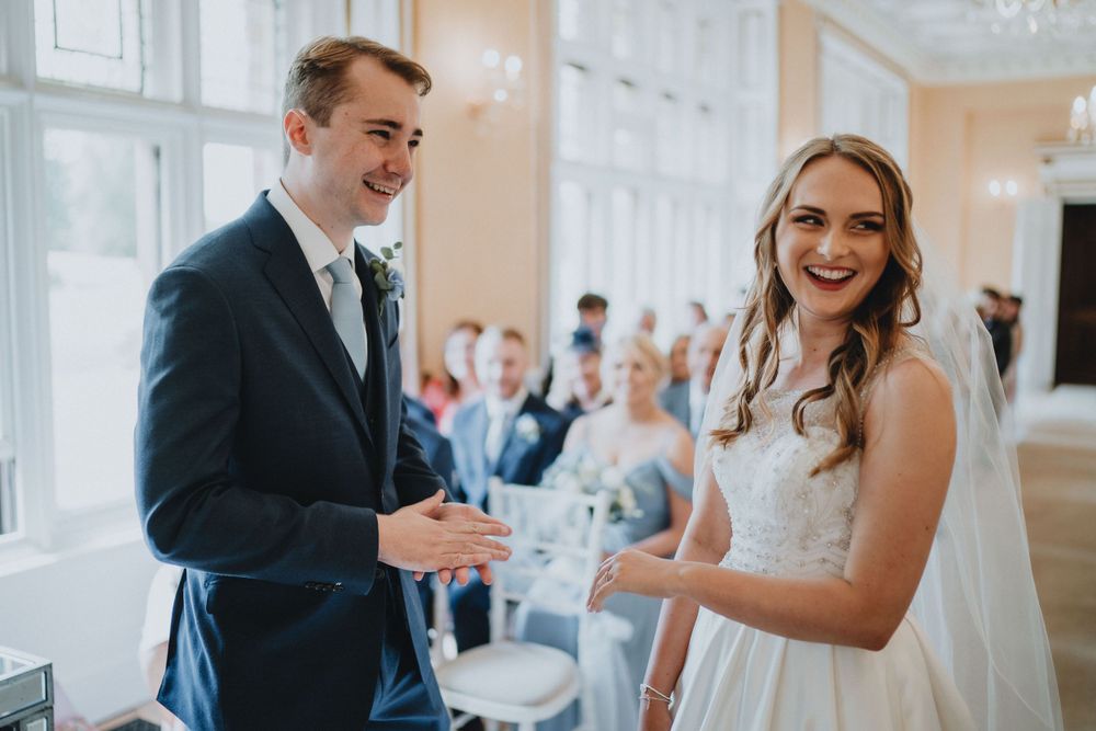 A bride and groom share a joyful moment during their wedding ceremony in an elegant indoor venue.