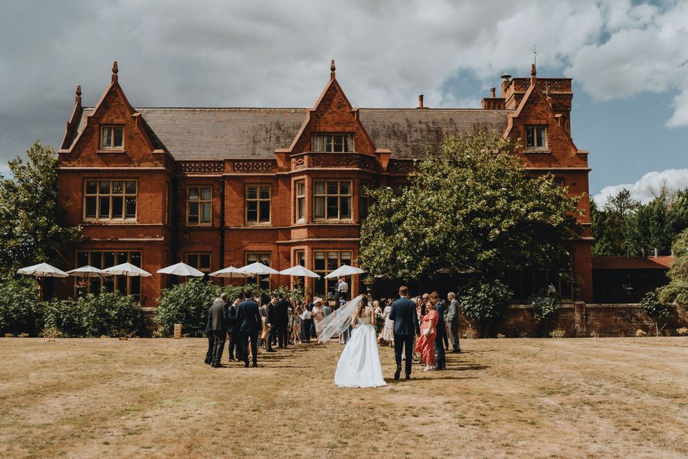 A wedding celebration outside Holmewood Hall a grand Victorian red brick manor house with guests gathered on the grounds.