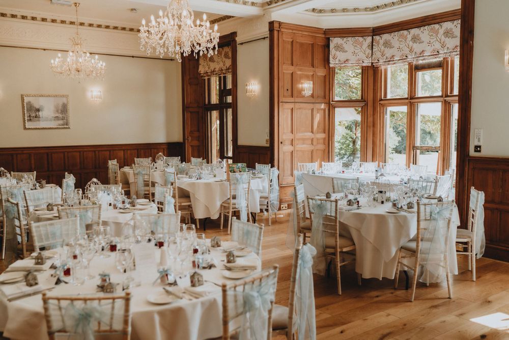 Elegant wedding reception at Holmewood Hall with crystal chandeliers and round tables set with white linens and classic table settings.