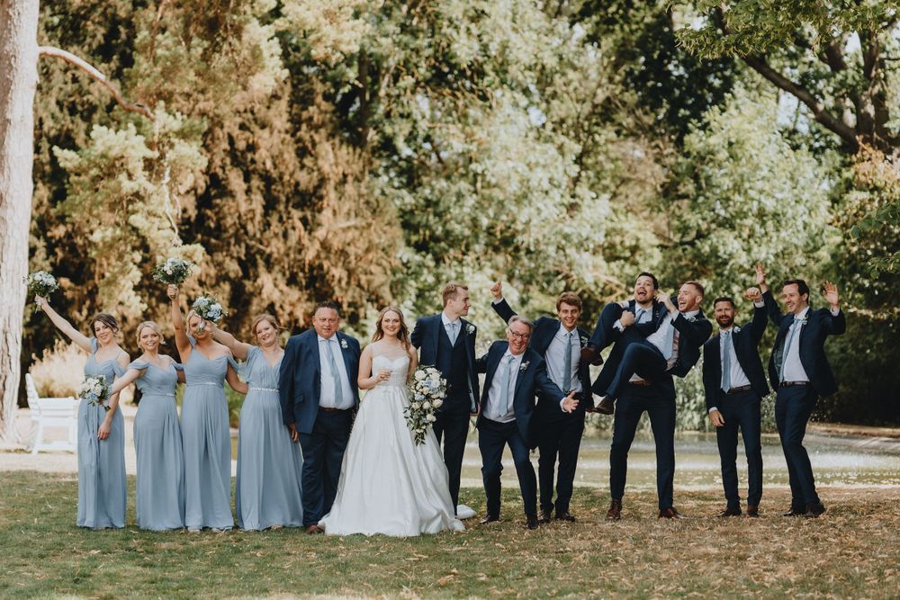 Wedding party poses outdoors at Holmewood Hall in elegant attire with bridesmaids in light blue dresses and groomsmen in dark suits.