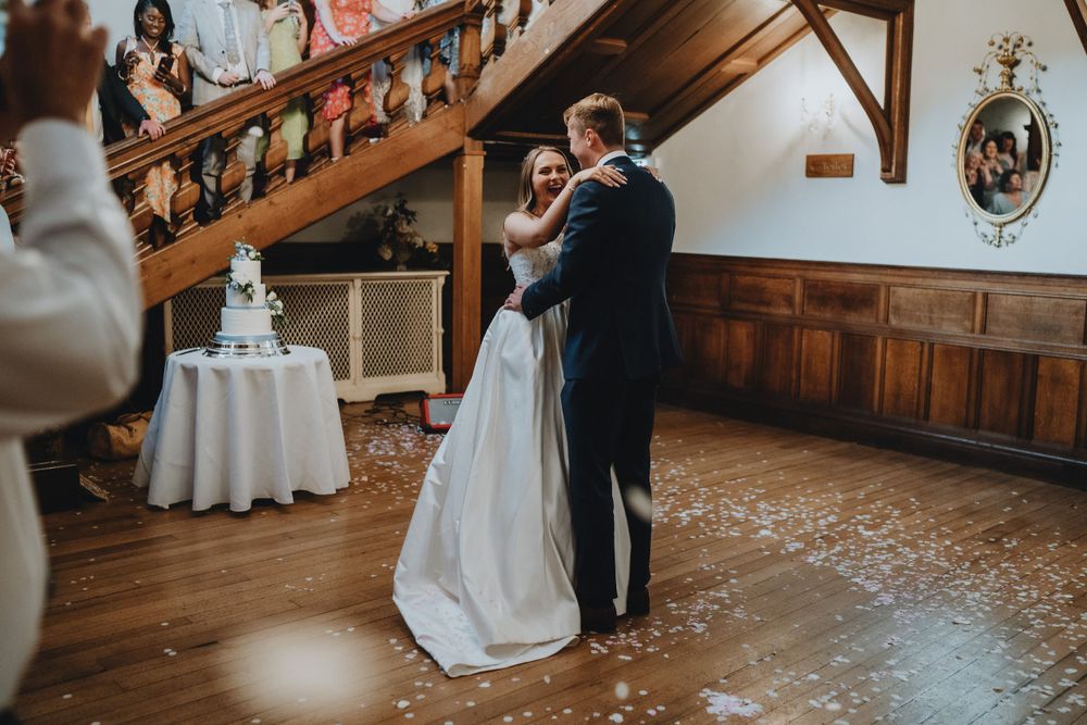 A couple shares their first dance at a rustic wedding reception venue with wooden walls and polished hardwood floors.