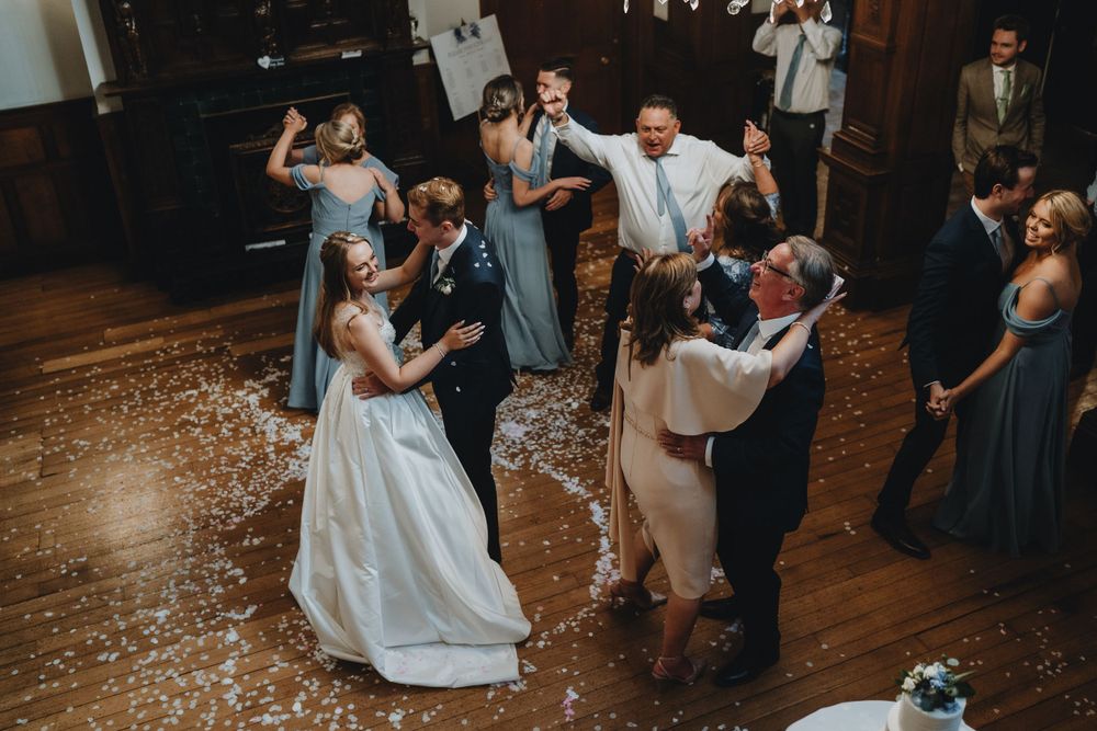 Guests enjoy dancing and celebrating at a wedding reception on a wood dance floor with flower petals scattered about.