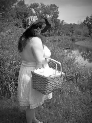 Person in white dress carrying wicker basket through tall grass near a pond.