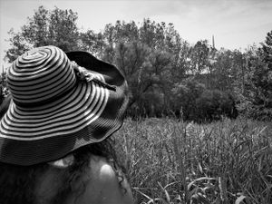Figure in striped sun hat photographed against natural landscape with trees.