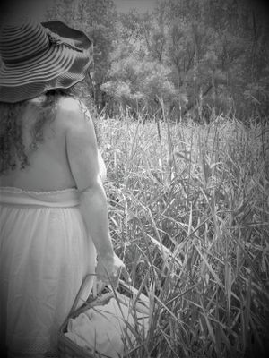Black and white photo of someone in flowing dress walking through tall reeds.
