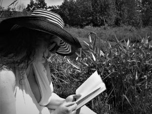 A dreamy monochrome scene of a person in a flowing dress reading outdoors on a summer day.
