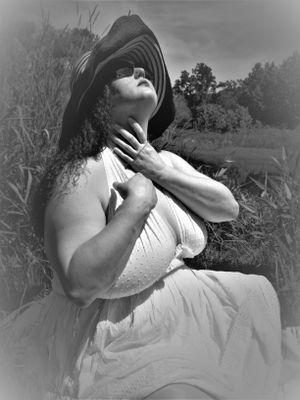 Dramatic black and white portrait of someone in white dress and wide-brimmed hat in nature.