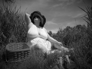 Black and white outdoor portrait showing someone in summer attire resting among tall grasses.