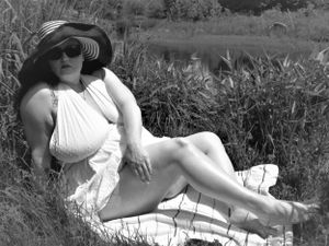 Artistic photograph of a figure in white dress and striped hat lounging in a natural setting.