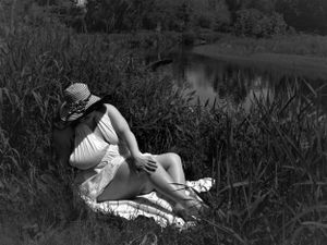 Nostalgic monochrome photo of a person relaxing outdoors in flowing white dress and sunhat.