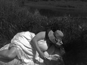 Atmospheric black and white photo of figure resting in grass wearing summer dress and hat.