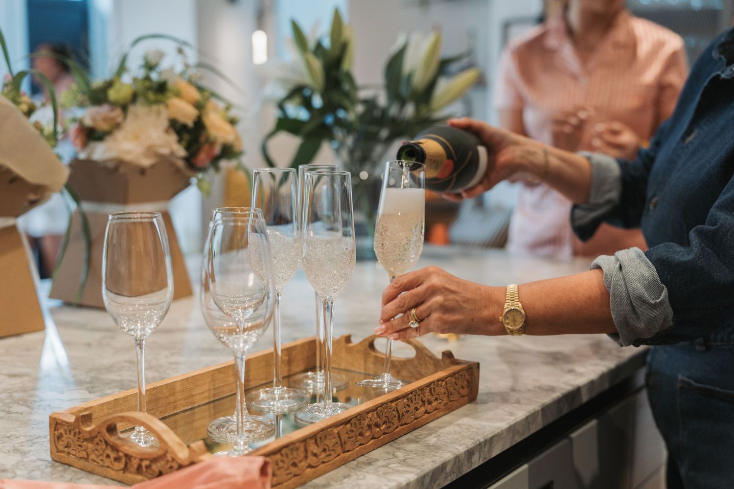 Elegant champagne glasses and cocktails arranged on a decorative wooden tray at a social gathering.