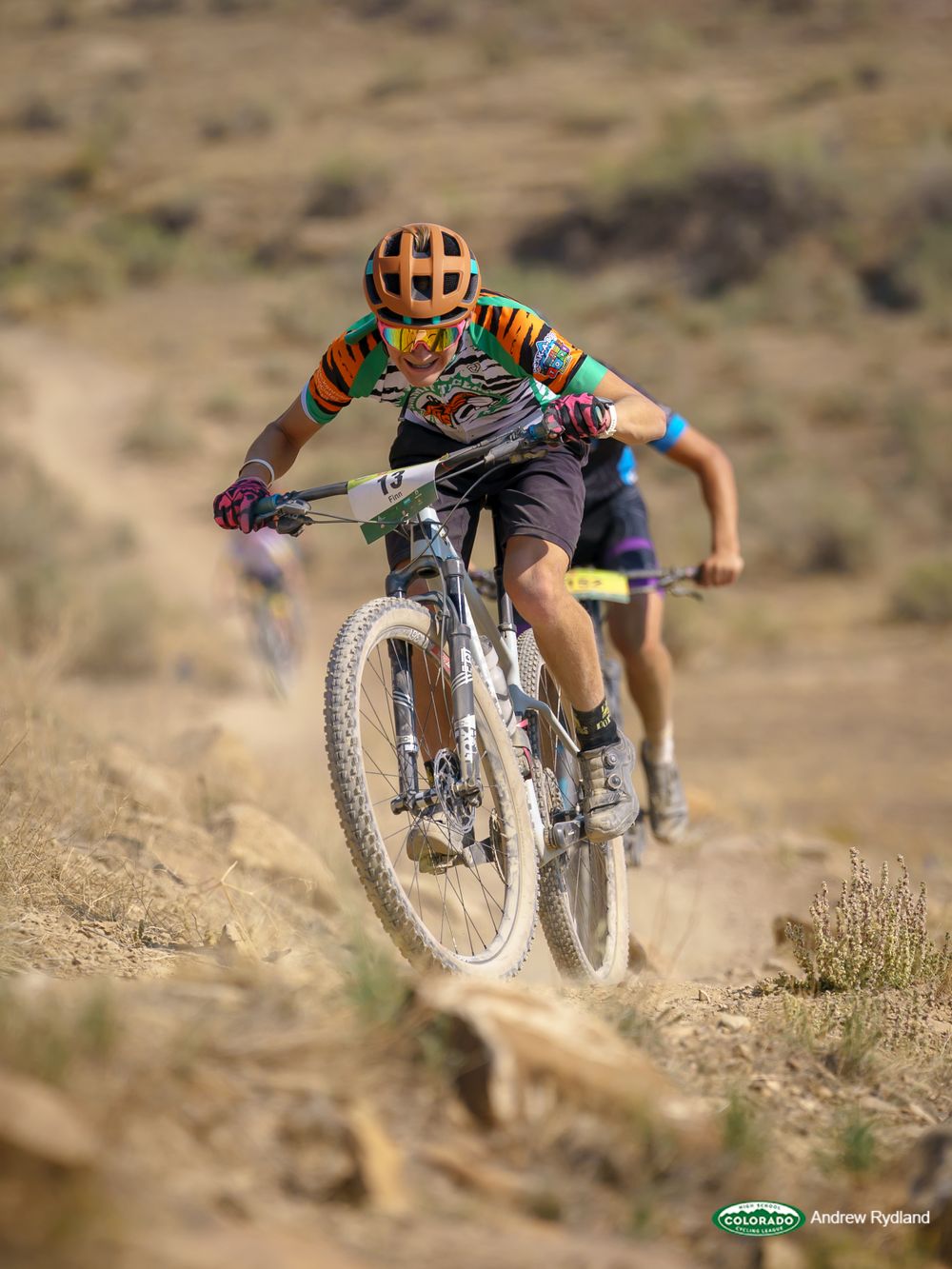 Mountain biker navigates rocky desert terrain wearing colorful helmet and jersey.