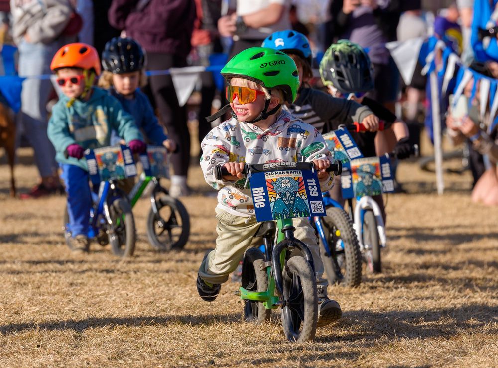 Young motocross riders race their dirt bikes across a dusty track during a youth competition event.