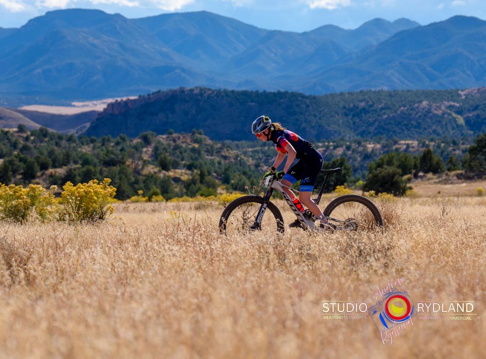 Mountain bike stands silhouetted against rugged mountain landscape with golden grass in the foreground.