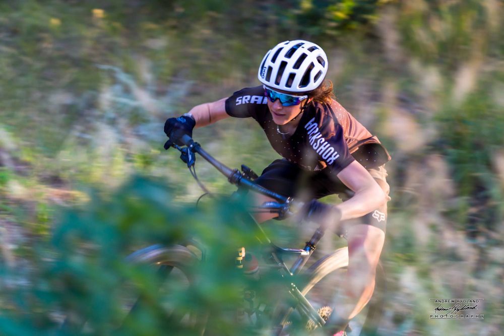 Mountain biker in motion rides through blurred natural terrain wearing protective gear.