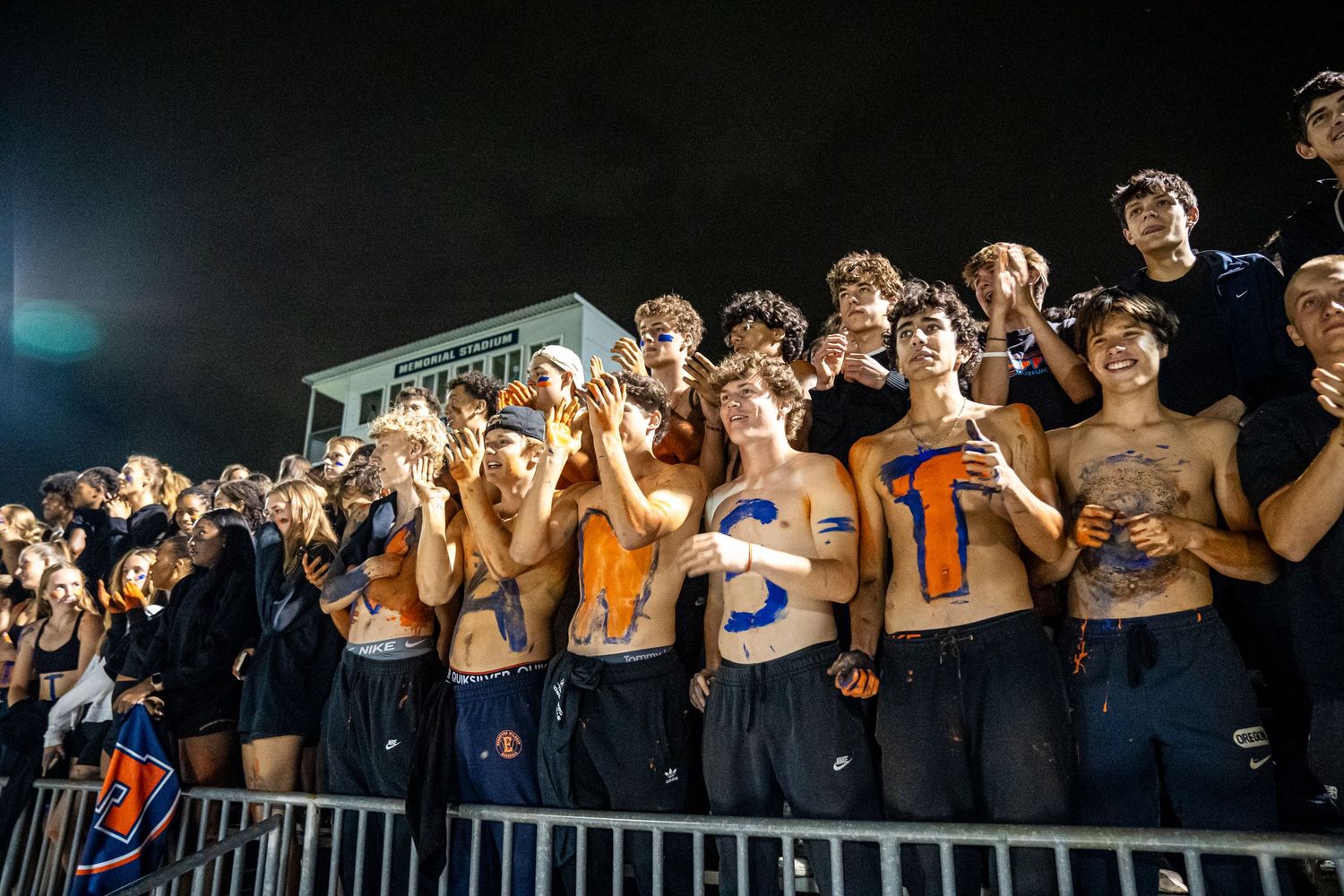 Student section fans cheering shirtless in the stands at a high school sporting event.