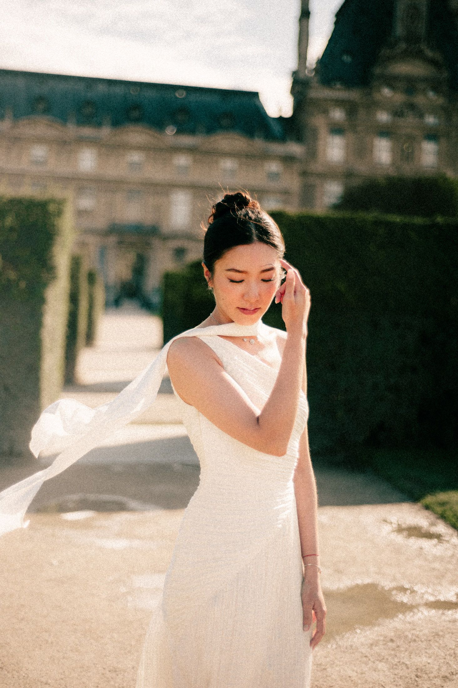 A bride in a sleeveless white dress poses against a historic building backdrop.