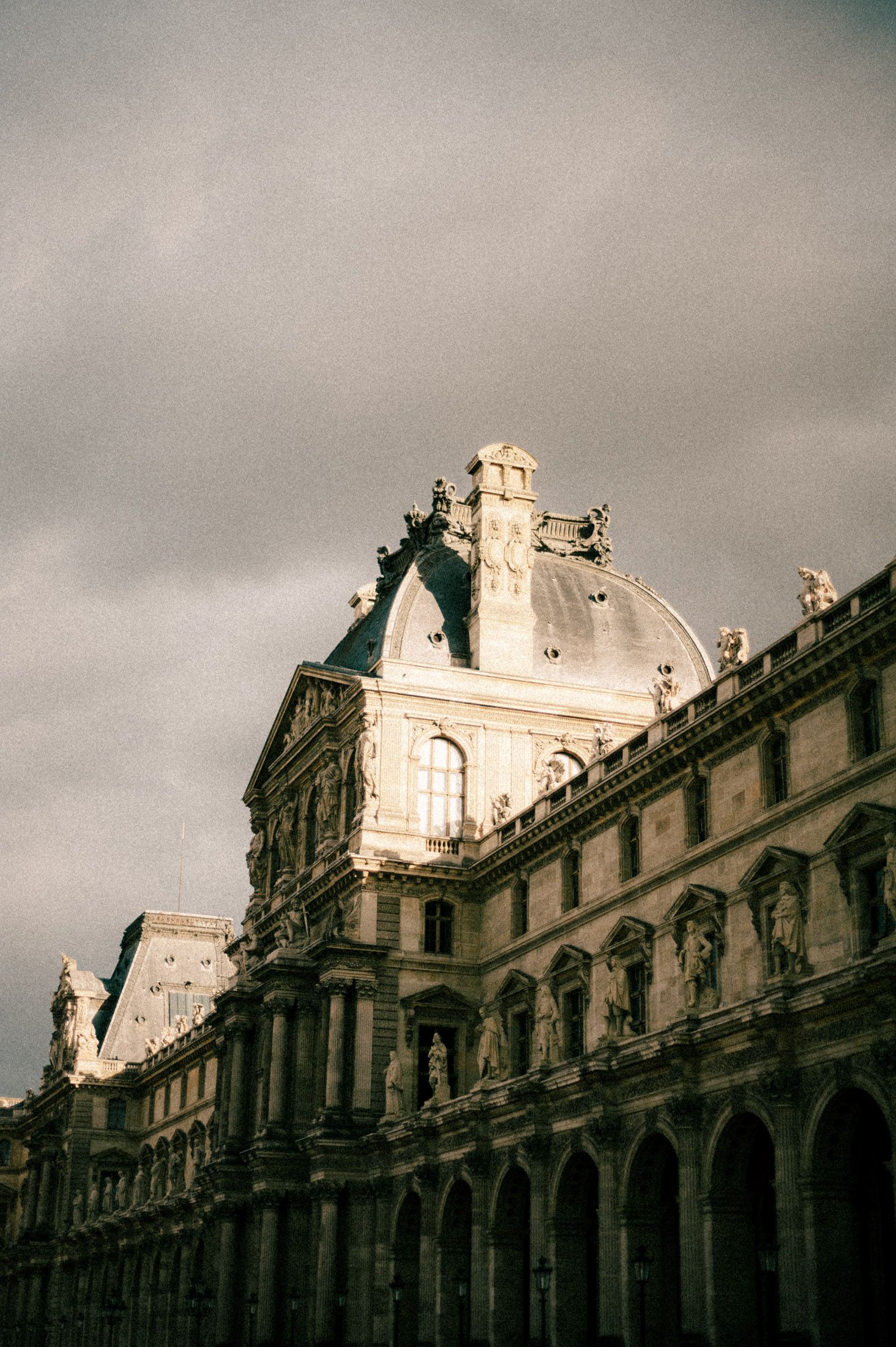 The ornate facade of the Louvre Museum in Paris under cloudy skies.
