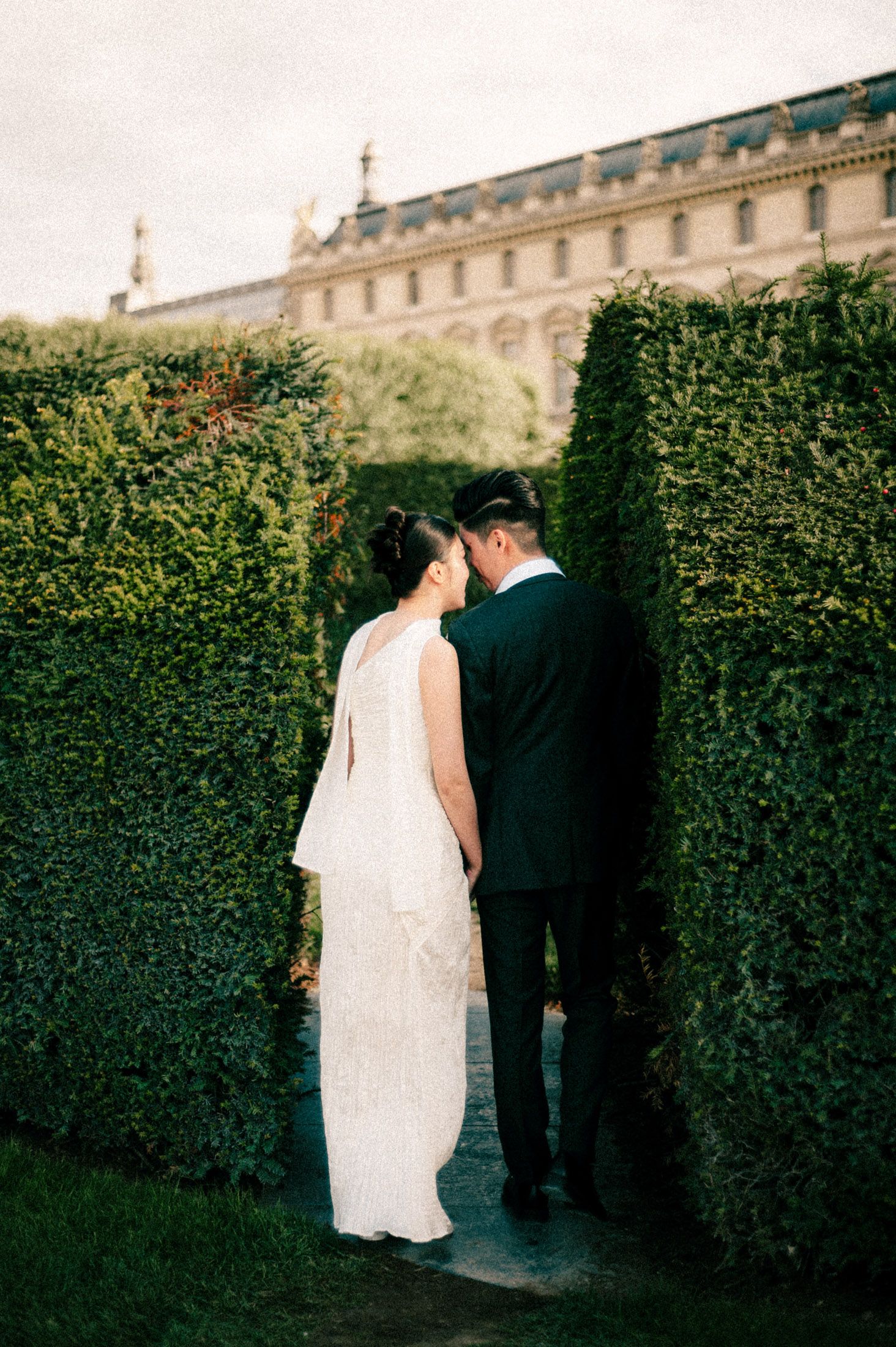 Newlyweds share an intimate moment between manicured garden hedges.