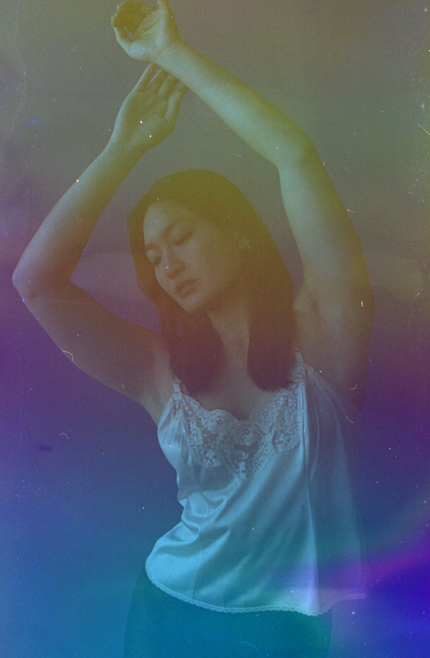 Dreamy dance pose in white camisole with colorful gradient lighting effects.
