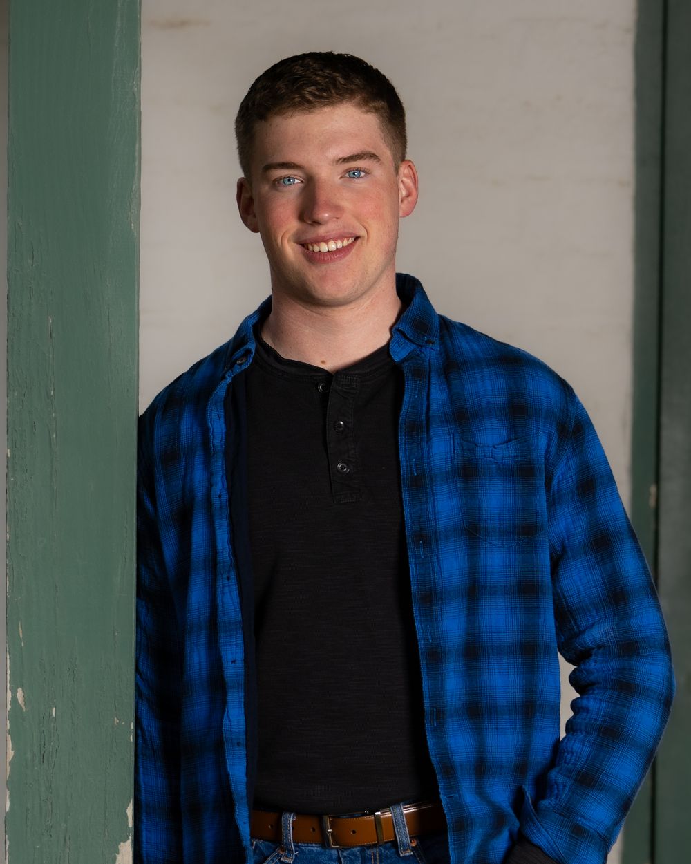 Young person wearing blue plaid flannel shirt stands in doorway.