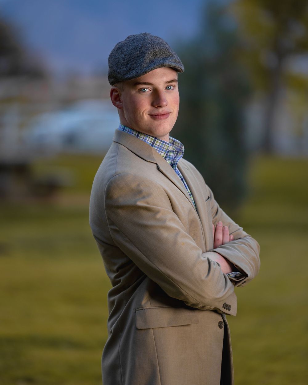 Stylish portrait in tan blazer and newsboy cap with arms crossed outdoors.
