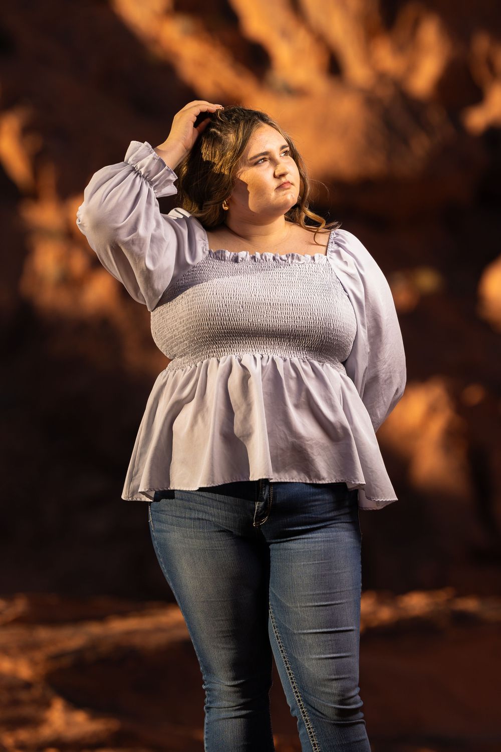 Portrait of a plus size model wearing a white ruffled peasant top and jeans against a warm brown backdrop.