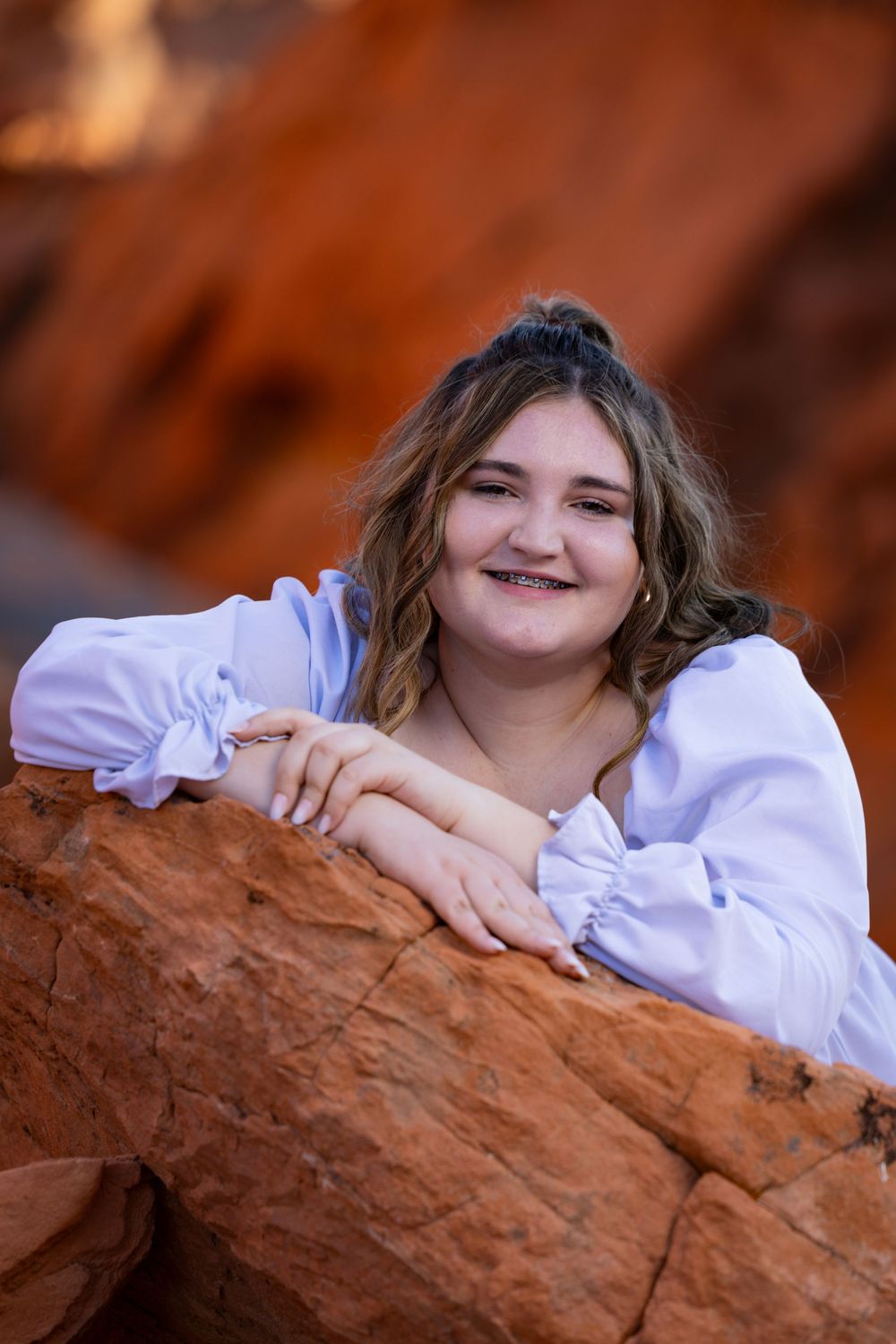 Person in white blouse rests on red rock formations during outdoor photo shoot in desert landscape.