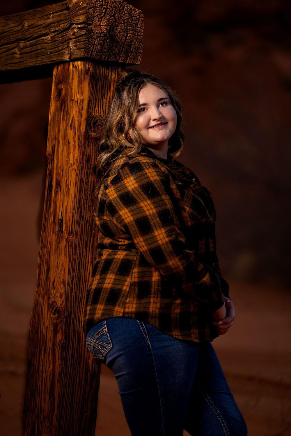 A rustic portrait against a wooden post shows someone in a plaid flannel shirt and jeans in warm autumn lighting.