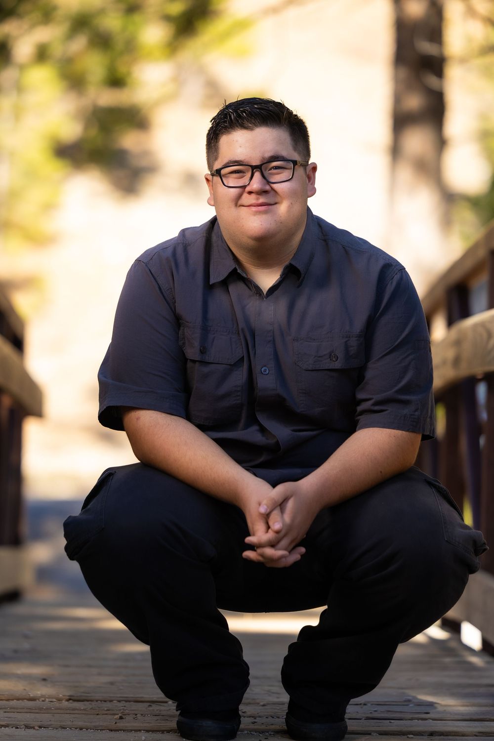 Person in navy polo shirt sitting on wooden boardwalk in natural outdoor setting with blurred background.