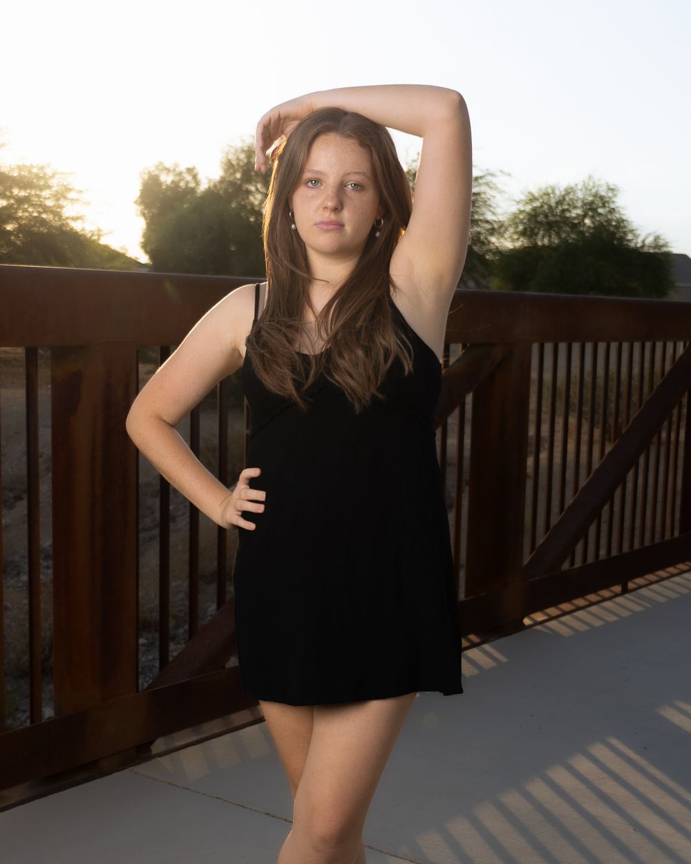A woman in a black top poses against a wooden deck railing during golden hour sunset.