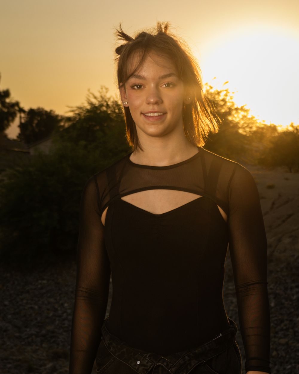 Person wearing a black mesh top with cutout detail poses outdoors during golden hour sunset.