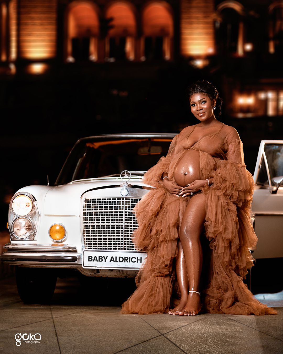 Maternity photo featuring pregnant woman in brown tulle gown beside vintage Mercedes.