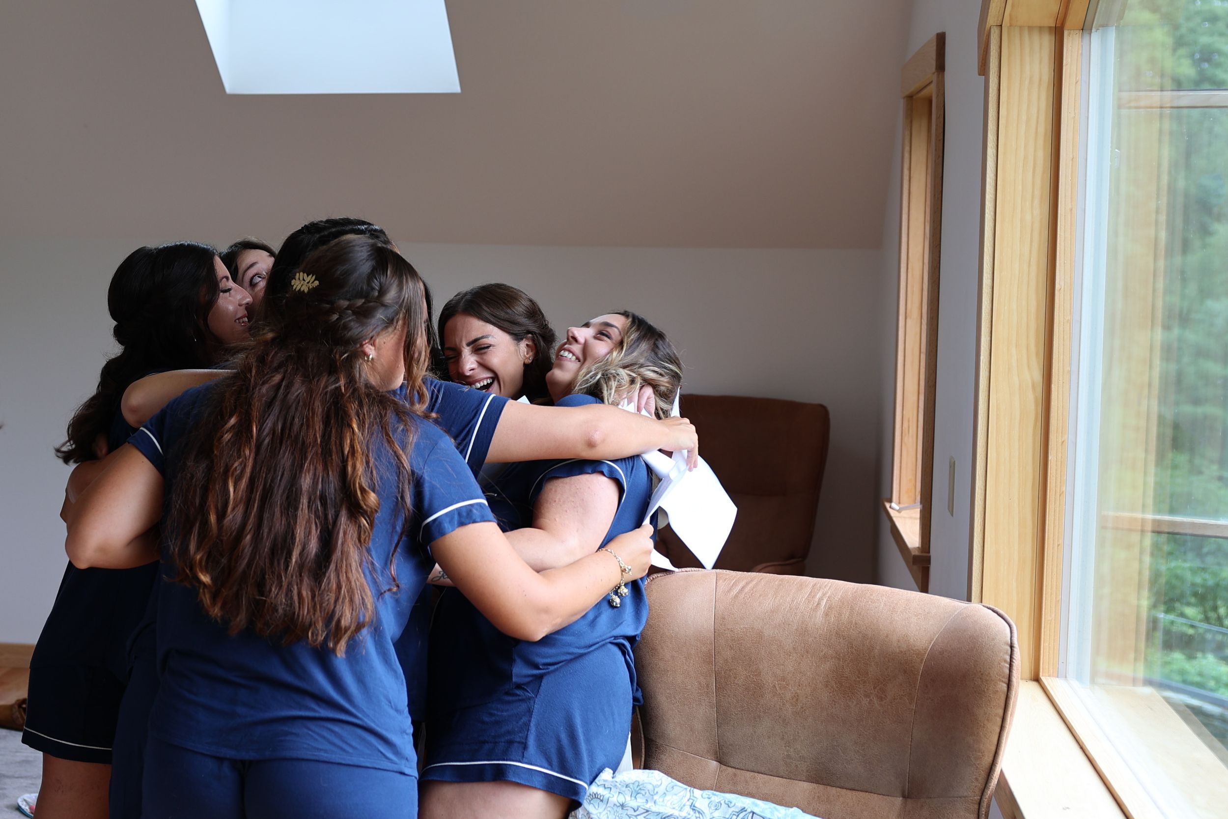 A group huddles together in an emotional embrace near a window in a room with natural lighting.