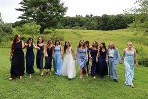Wedding party in mix of navy and light blue dresses poses on a grassy hillside.