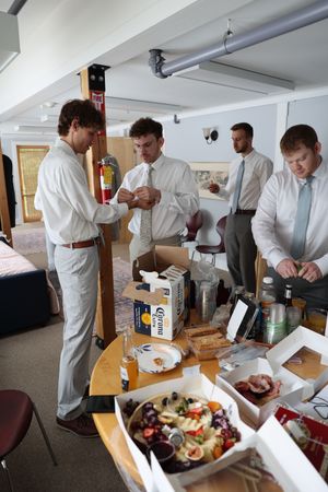 People preparing food and drinks at a casual gathering with snacks and beverages on a table.