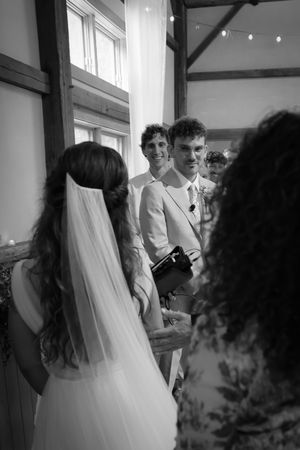 Black and white photo of wedding reception with guests gathered under string lights.