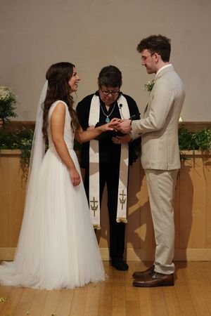 An exchange of rings takes place during a wedding ceremony on a wooden floor with simple decor.