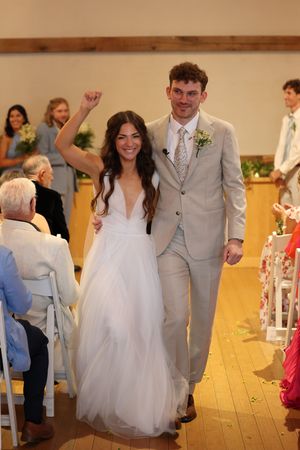 Wedding reception featuring elegant gowns and suits as couples move along an indoor aisle in a bright venue.