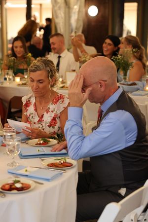 Wedding reception dinner guests seated at tables with white linens and floral centerpieces.