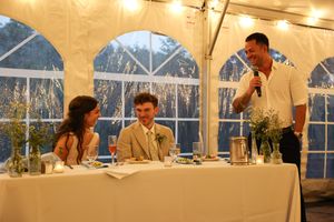 Dining scene in a white tent with guests at tables and staff providing service.