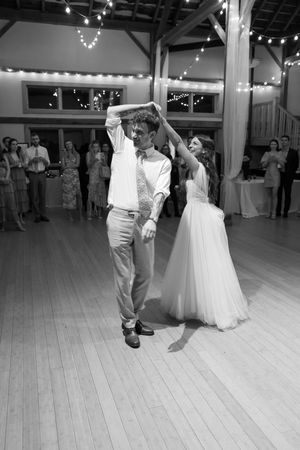 Couples dance under string lights in a spacious reception hall with wooden floors.