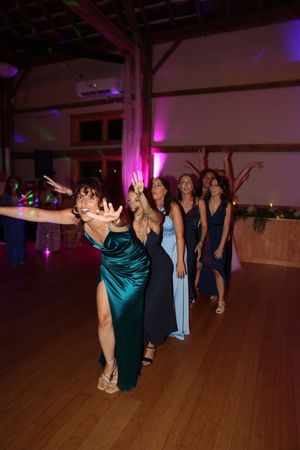 Wedding party dancing on a wooden dance floor illuminated by purple and blue lighting at a reception.