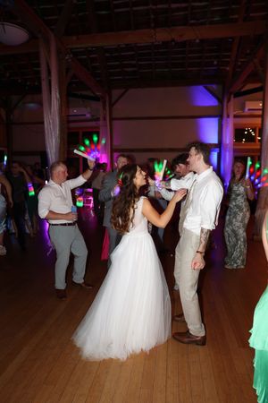 Wedding reception party on a wooden dance floor with guests dancing under colorful neon lights.