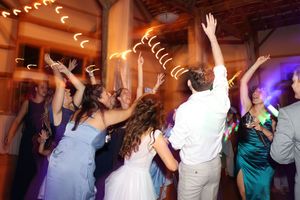 Wedding guests dance with raised arms under colorful party lighting at an indoor reception.