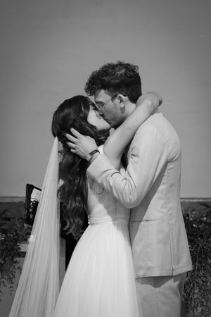 A romantic black and white portrait captures a tender kiss between newlyweds in formal wedding attire.