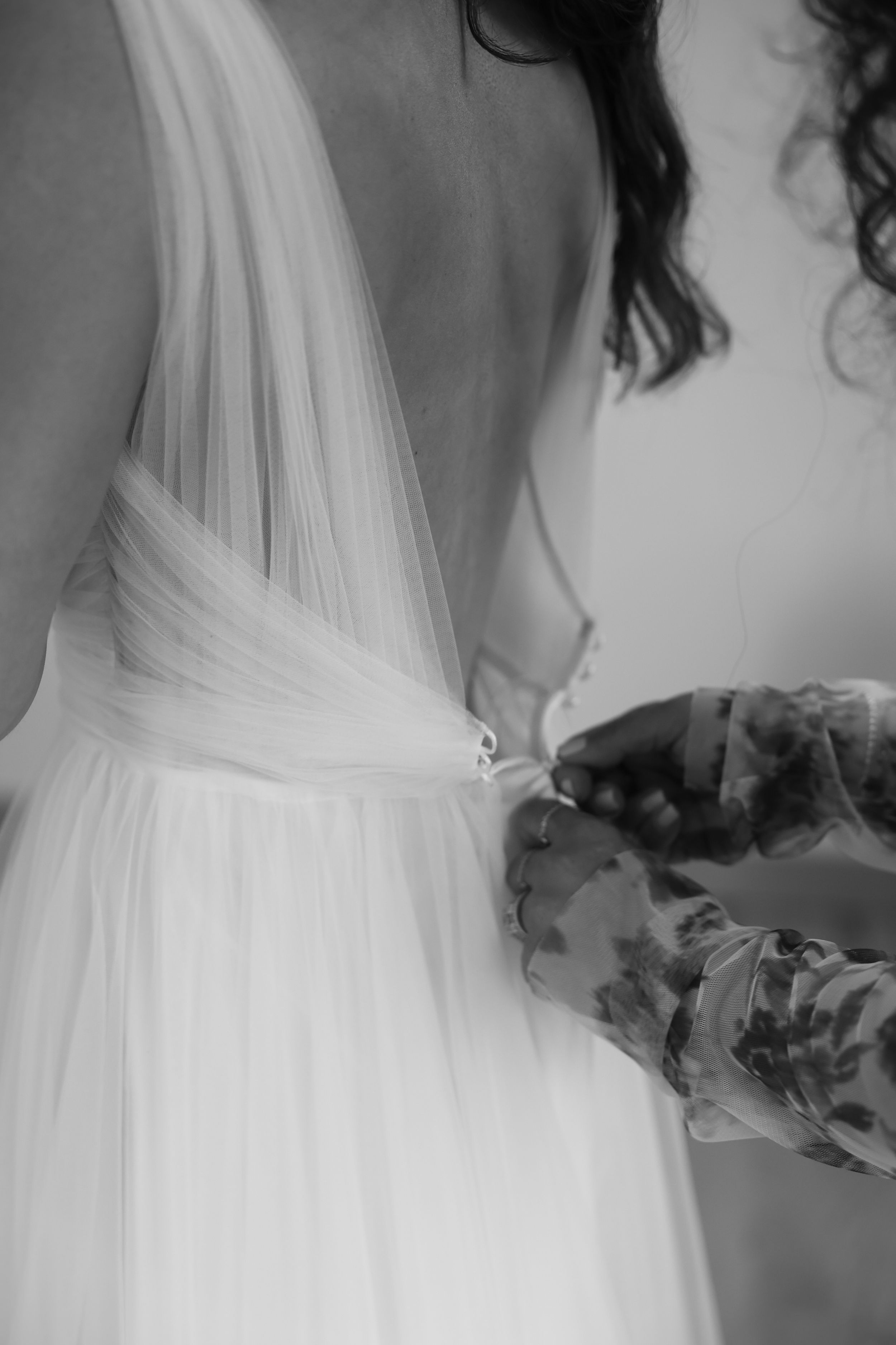 A close-up black and white shot of hands adjusting the waistline of a flowing white wedding dress.