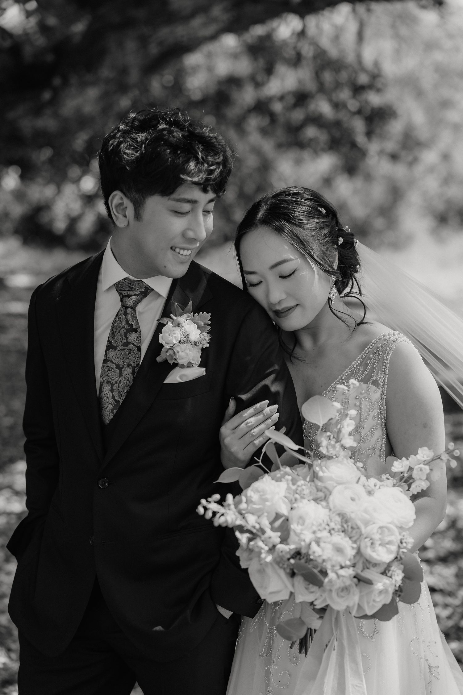 A black and white wedding portrait of a couple in traditional formal attire with bride holding a bouquet of white flowers.